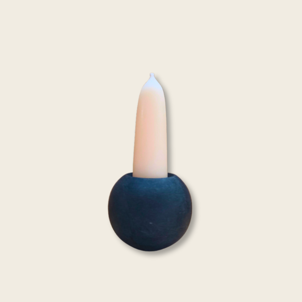 stubby white candle in a black stone ball candle holder with a beige background