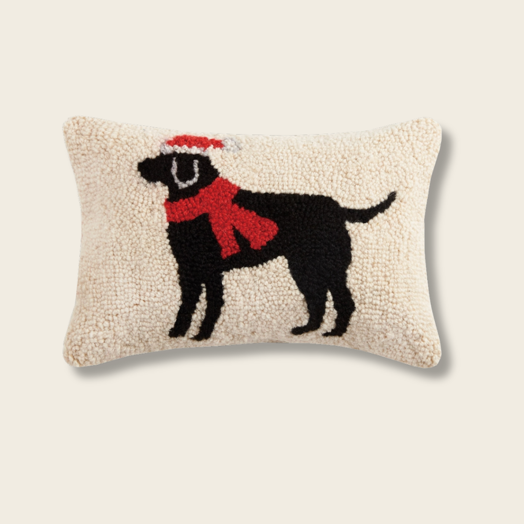 Decorative pillow with a black dog silhouette wearing a red scarf and a Santa hat on a beige background.