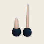 short stubby candle and a tall taper candle in a matching pair of black stone candle holders with a beige background