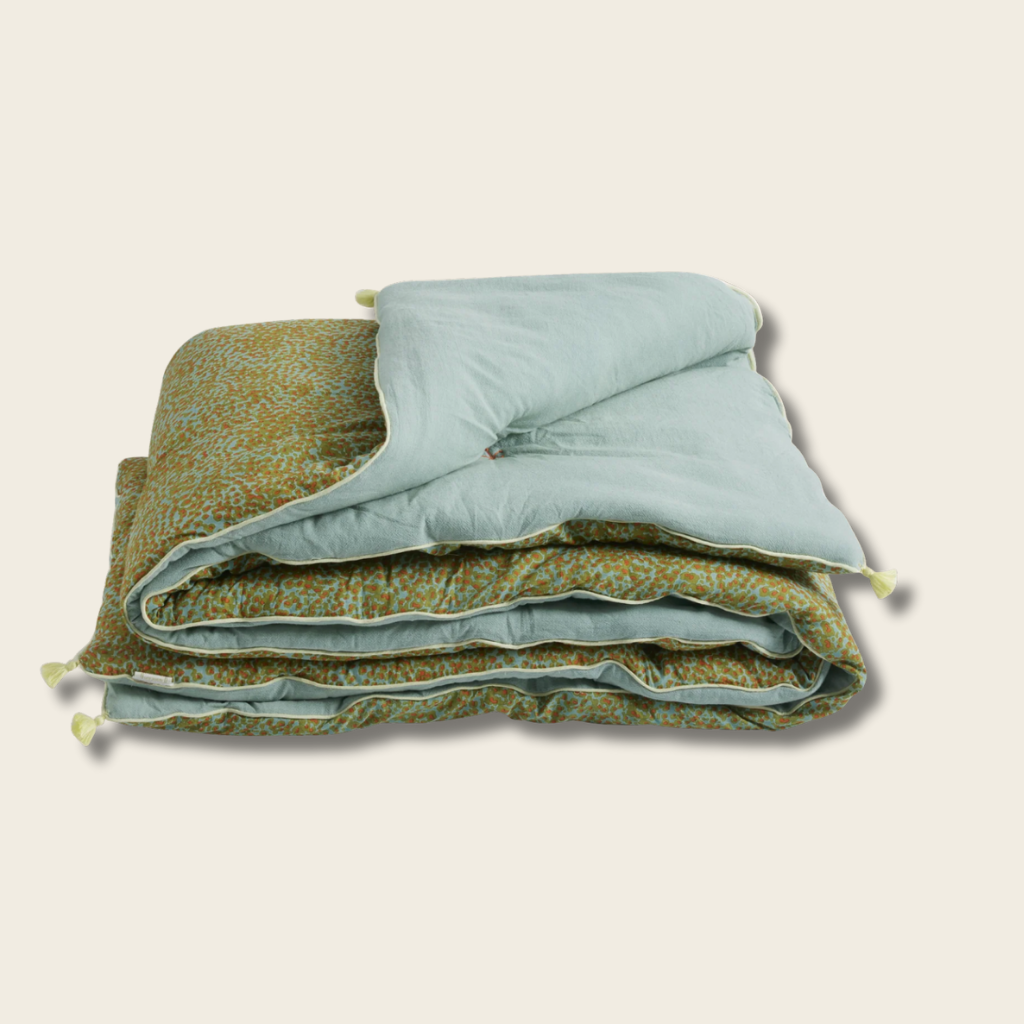 Folded quilt with green floral pattern and light blue interior on a beige background