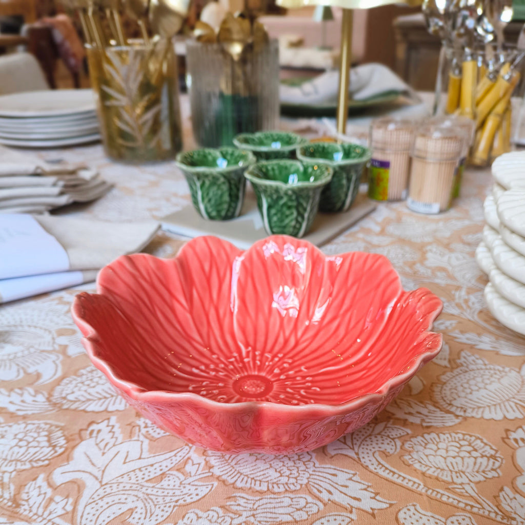 Coral ceramic bowl on a patterned tablecloth with green cups and plates in the background.
