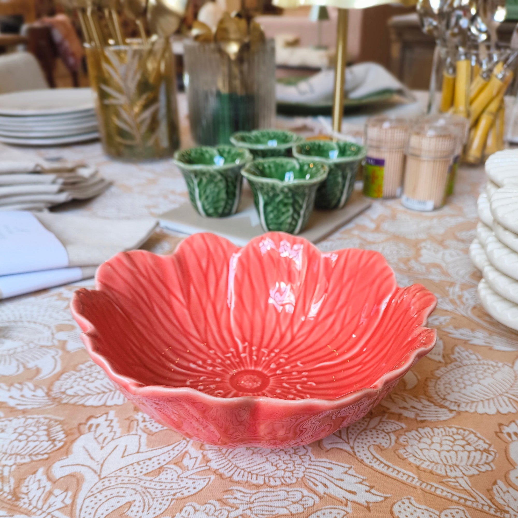 Coral ceramic bowl on a patterned tablecloth with green cups and plates in the background.