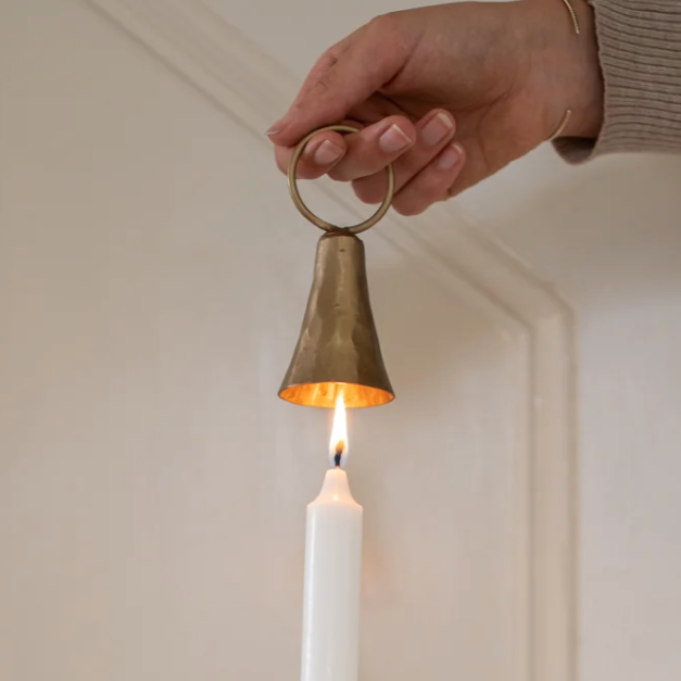 Hand holding a brass candle snuffer over a lit candle against a neutral background