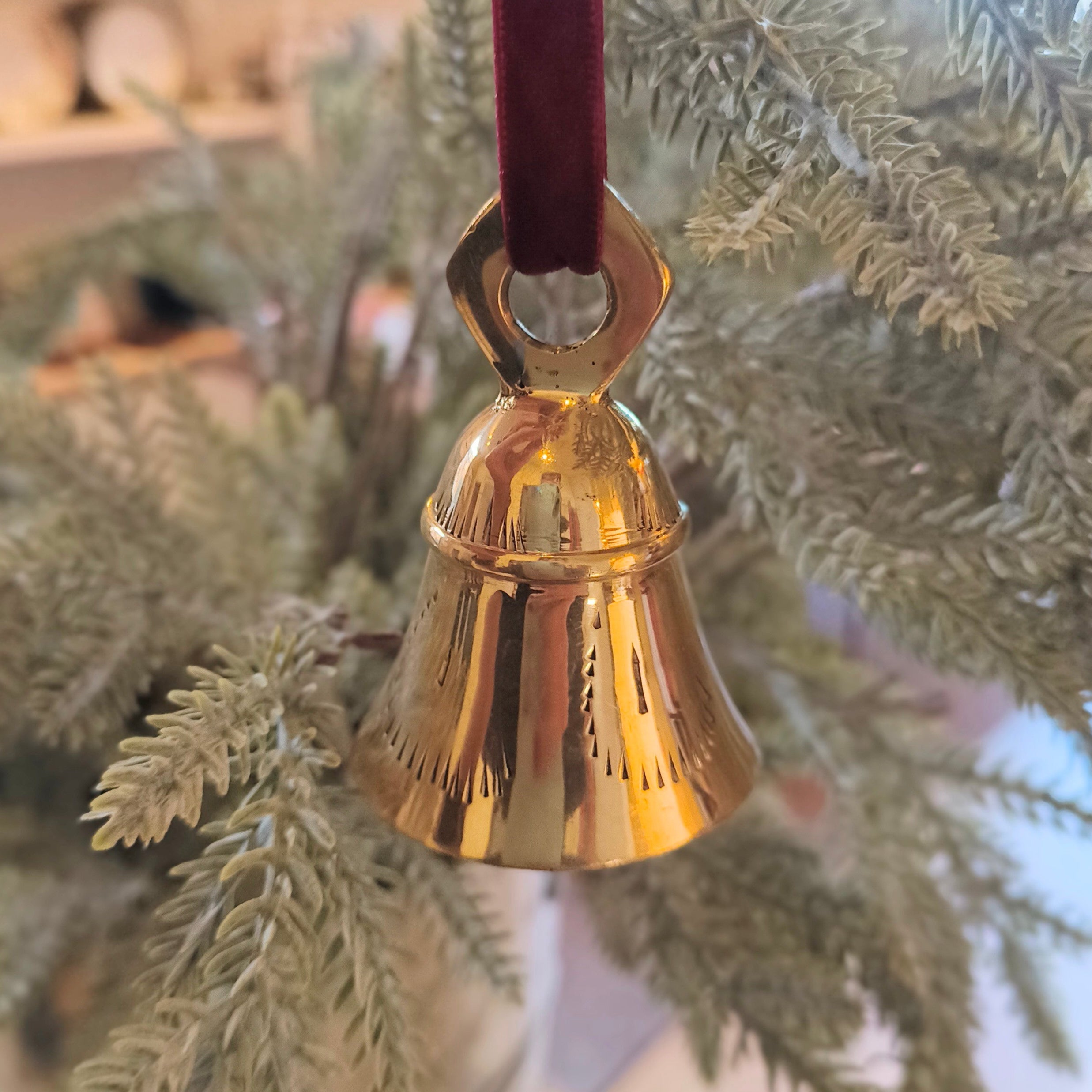 Gold bell ornament on a red ribbon hanging on a Christmas tree.
