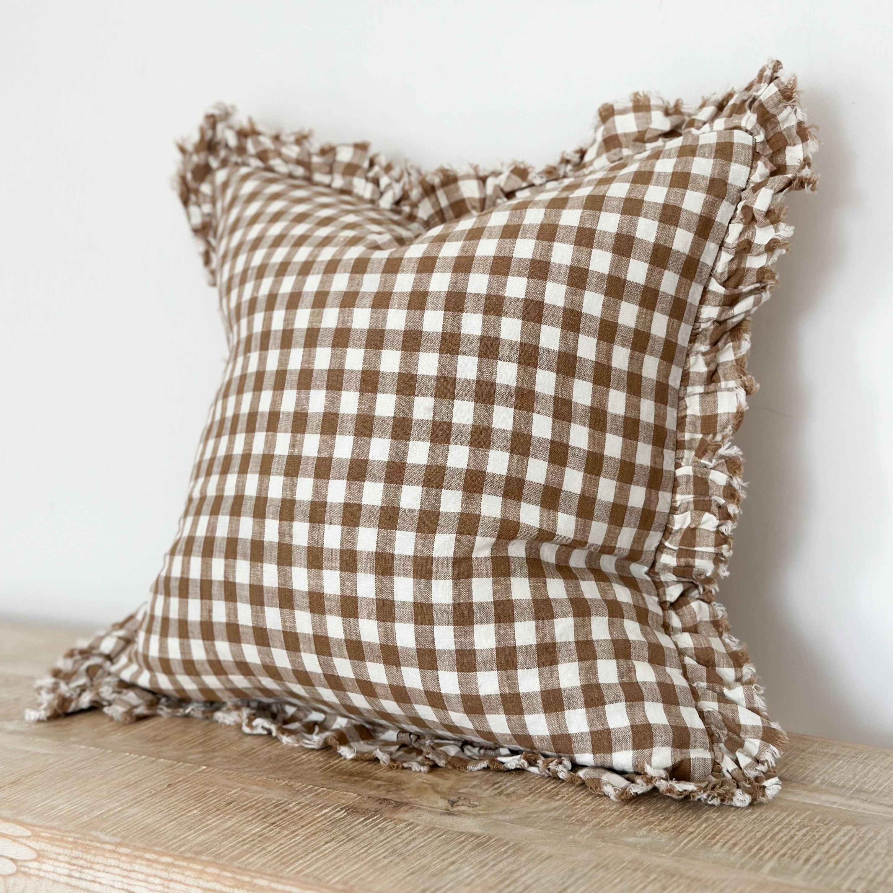 Brown and white checkered pillow with ruffled edges on a wooden surface.
