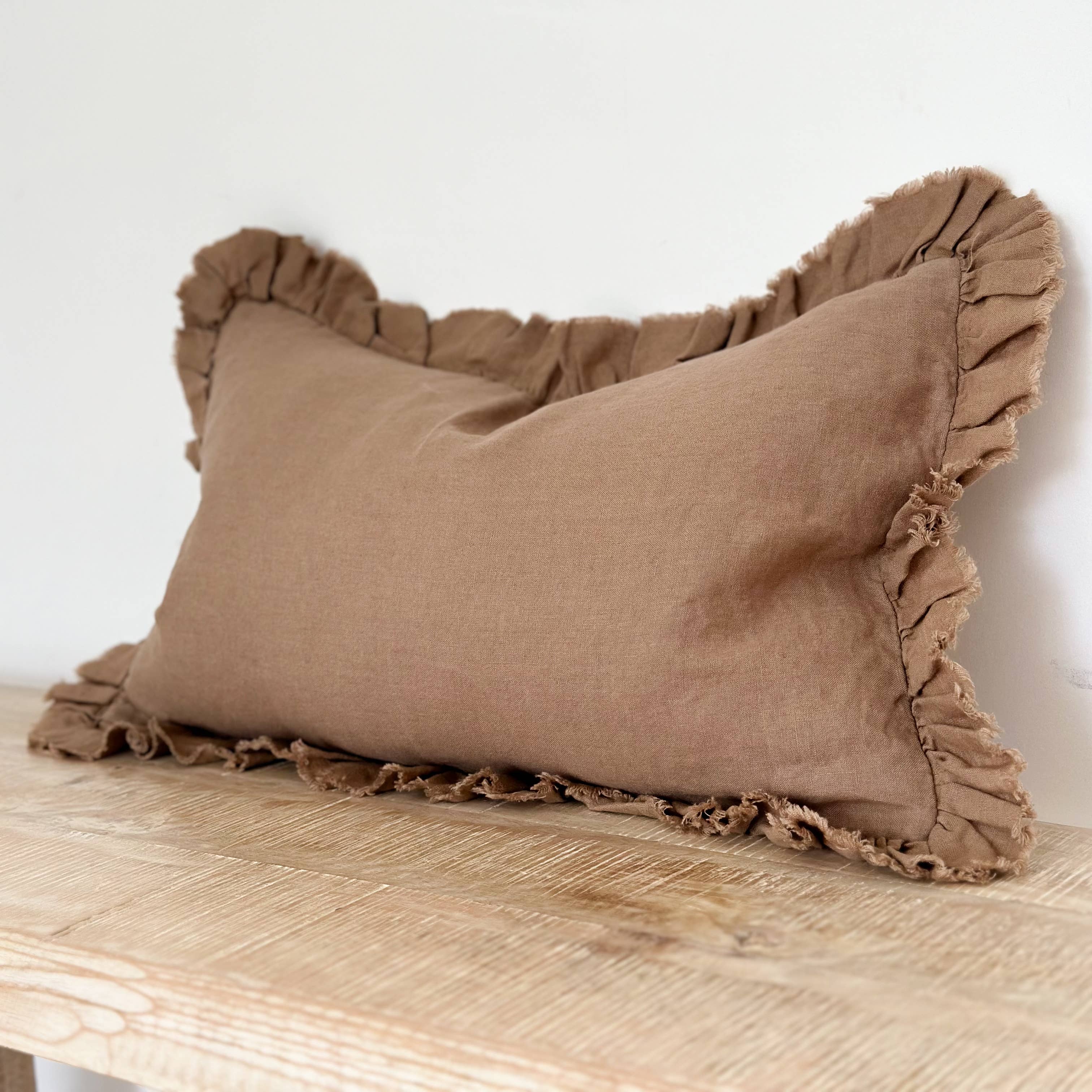 Brown pillow with ruffled edges on a wooden surface against a white wall