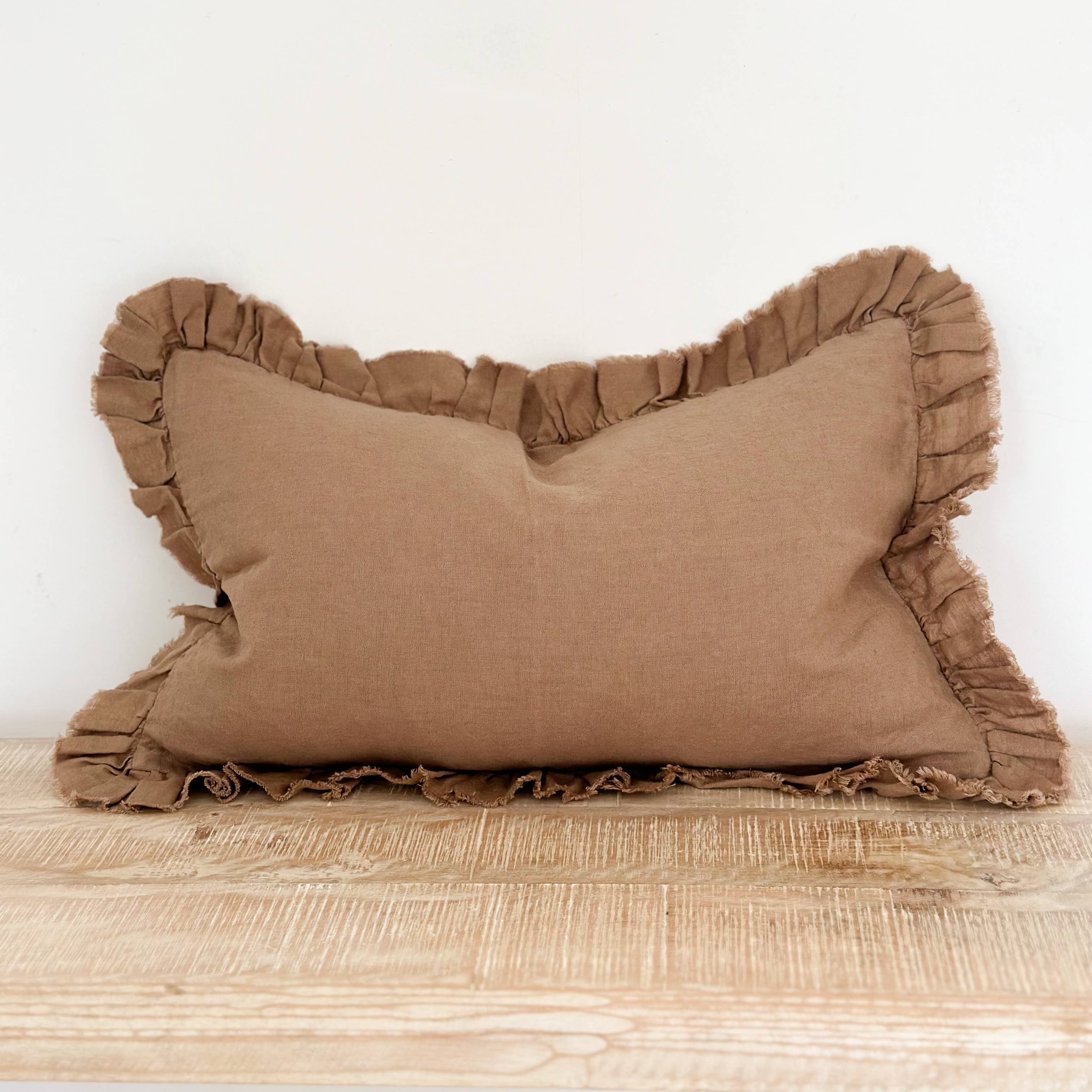 Brown pillow with ruffled edges on a wooden surface against a white wall