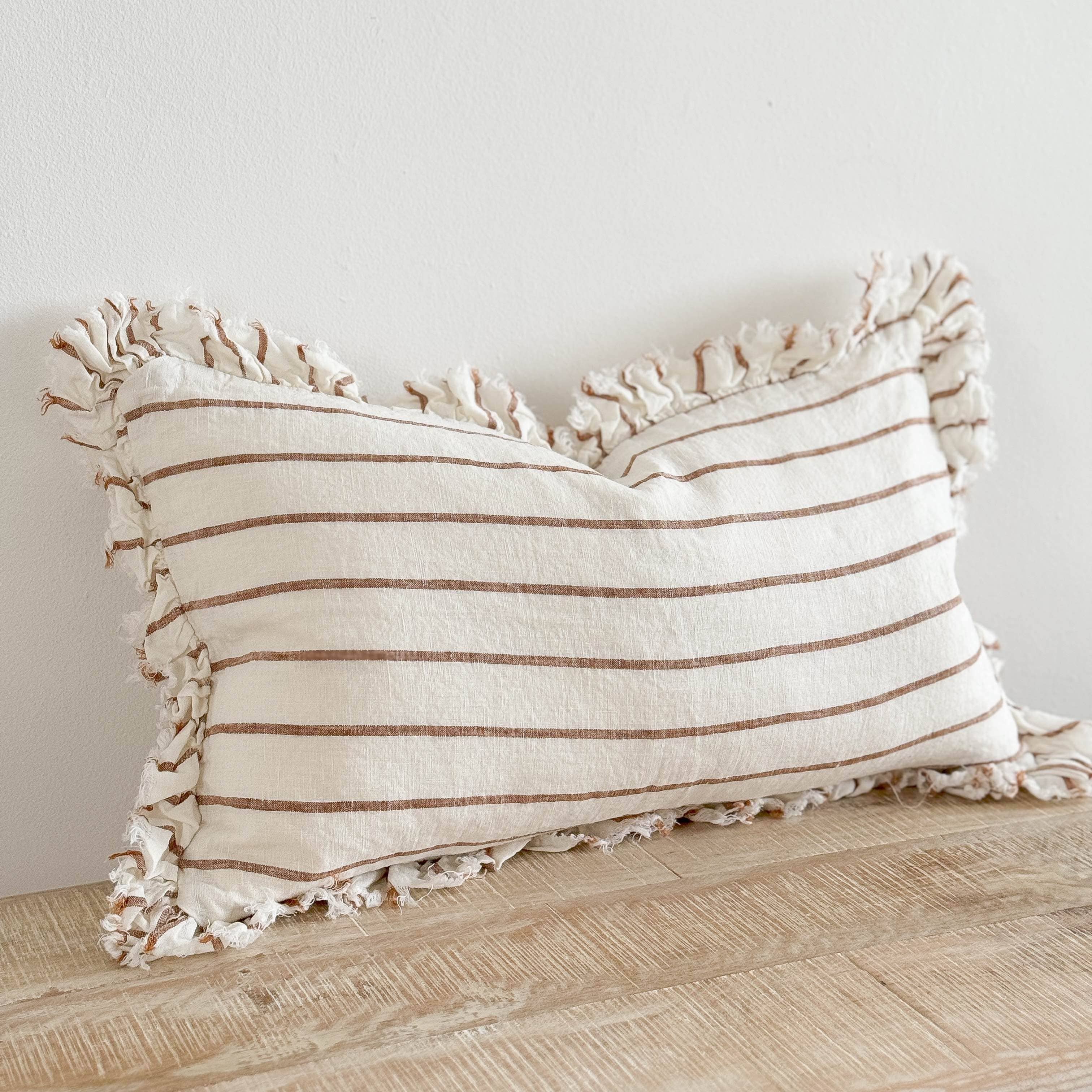 Striped pillow with tassels on a wooden surface against a white wall