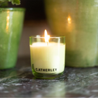 Catherley candle burning on a stone surface with green containers in the background