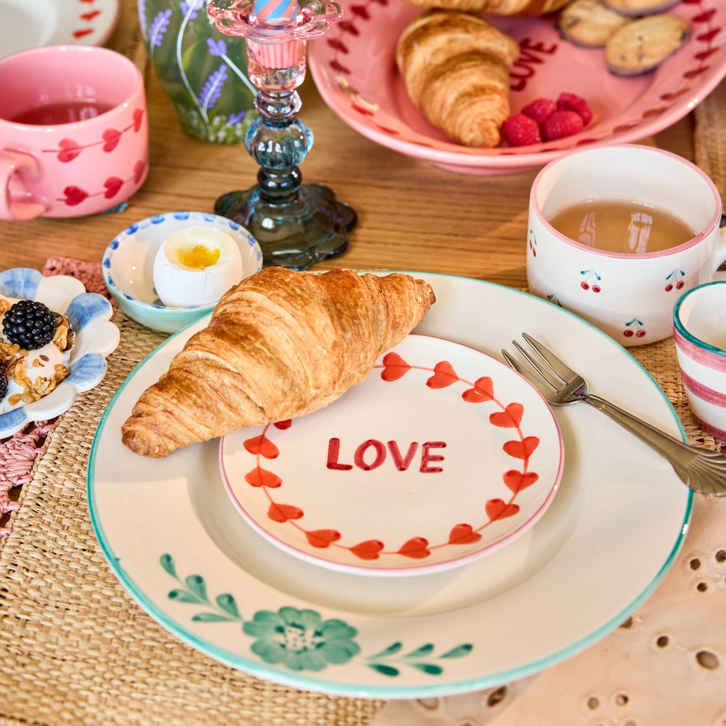 Breakfast table setting with croissants, eggs, and a 'LOVE' plate on a wooden table.