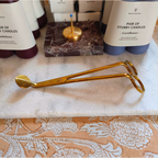 Gold plated stainless steel wick trimmer on a marble stone in front of candles. 