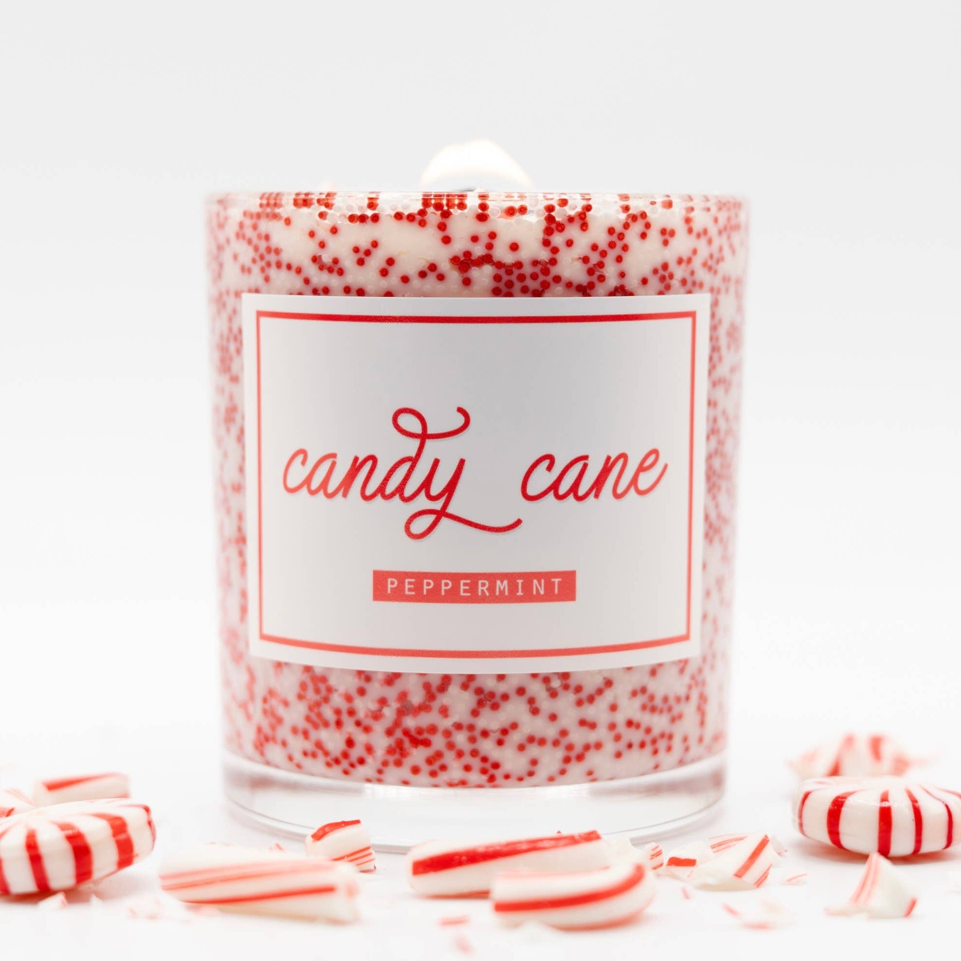 Candle labeled 'candy cane' with red and white speckles, surrounded by candy canes on a white background.