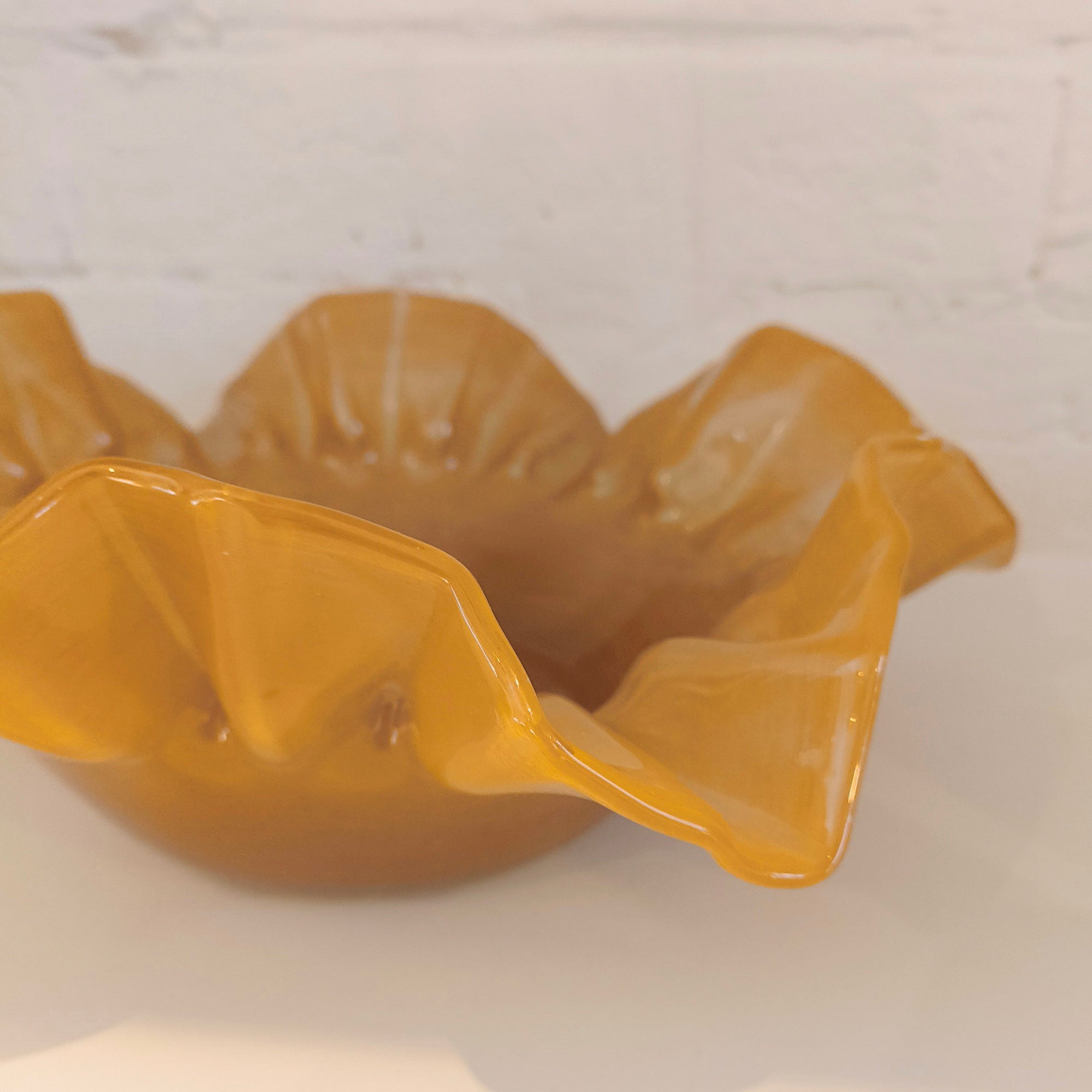 Caramel ceramic bowl with scalloped edge on a light background