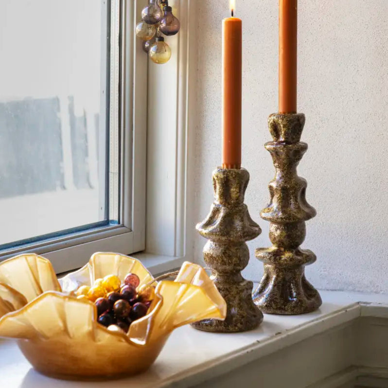 Decorative candles in ornate holders on a windowsill with a bowl of fruit.