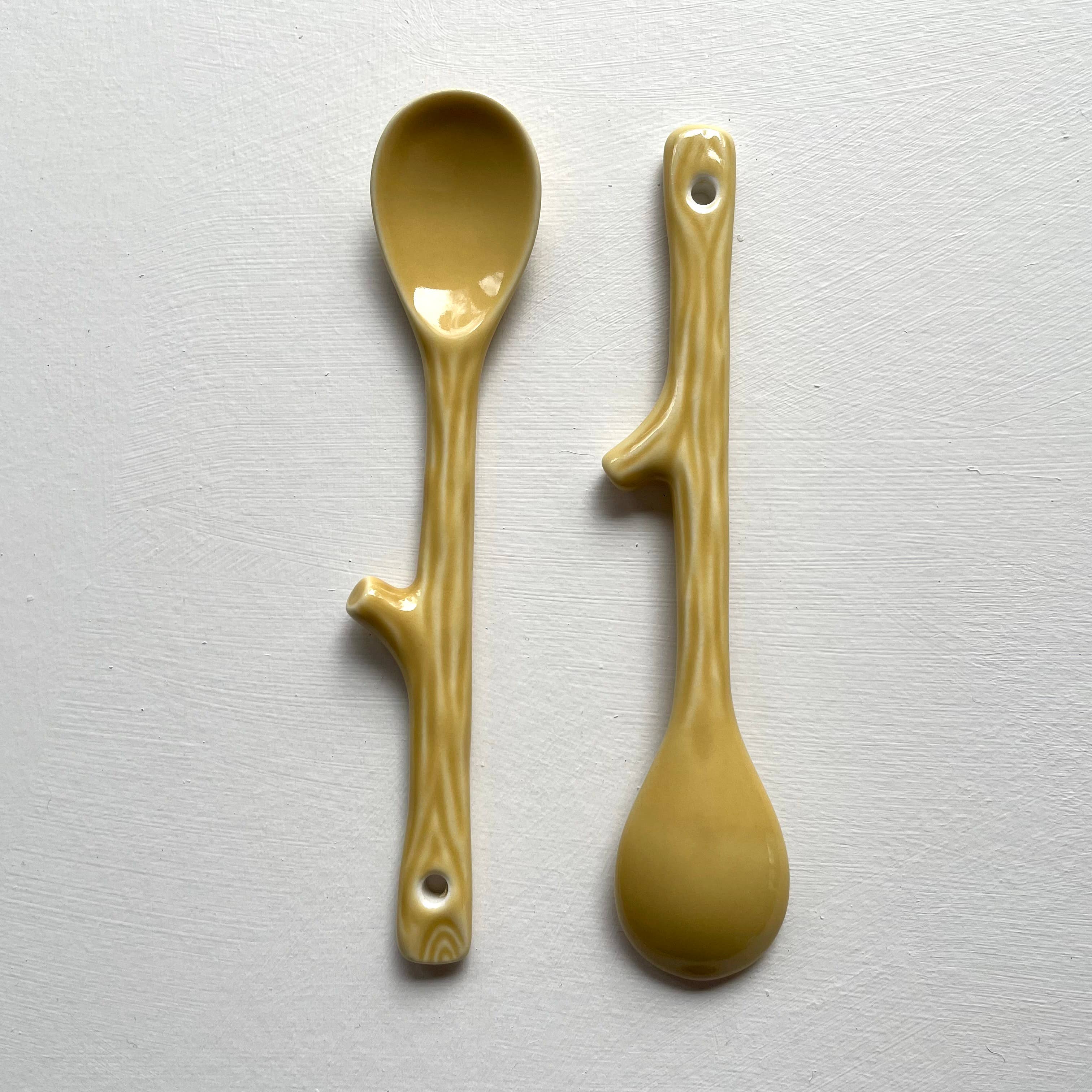 Two ceramic spoons with branch-like handles on a light gray background