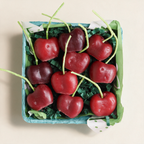 Set of ten cherry-shaped beeswax candles in a berry basket on a cream background
