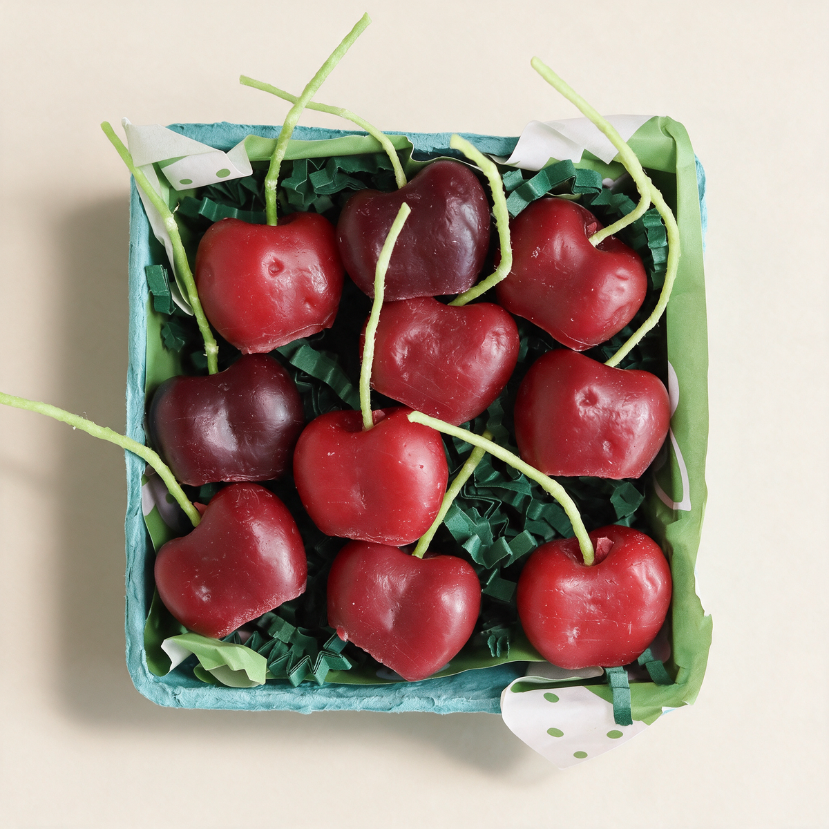 Set of ten cherry-shaped beeswax candles in a berry basket on a cream background