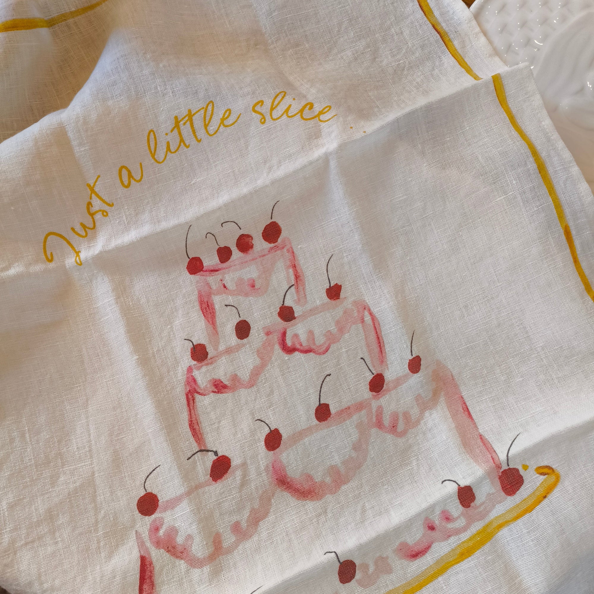 tea towel with cherry design and text 'Just a little slice' on a wooden surface