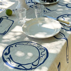 Table setting with white plates, glasses, and a decorative tablecloth featuring blue patterns.