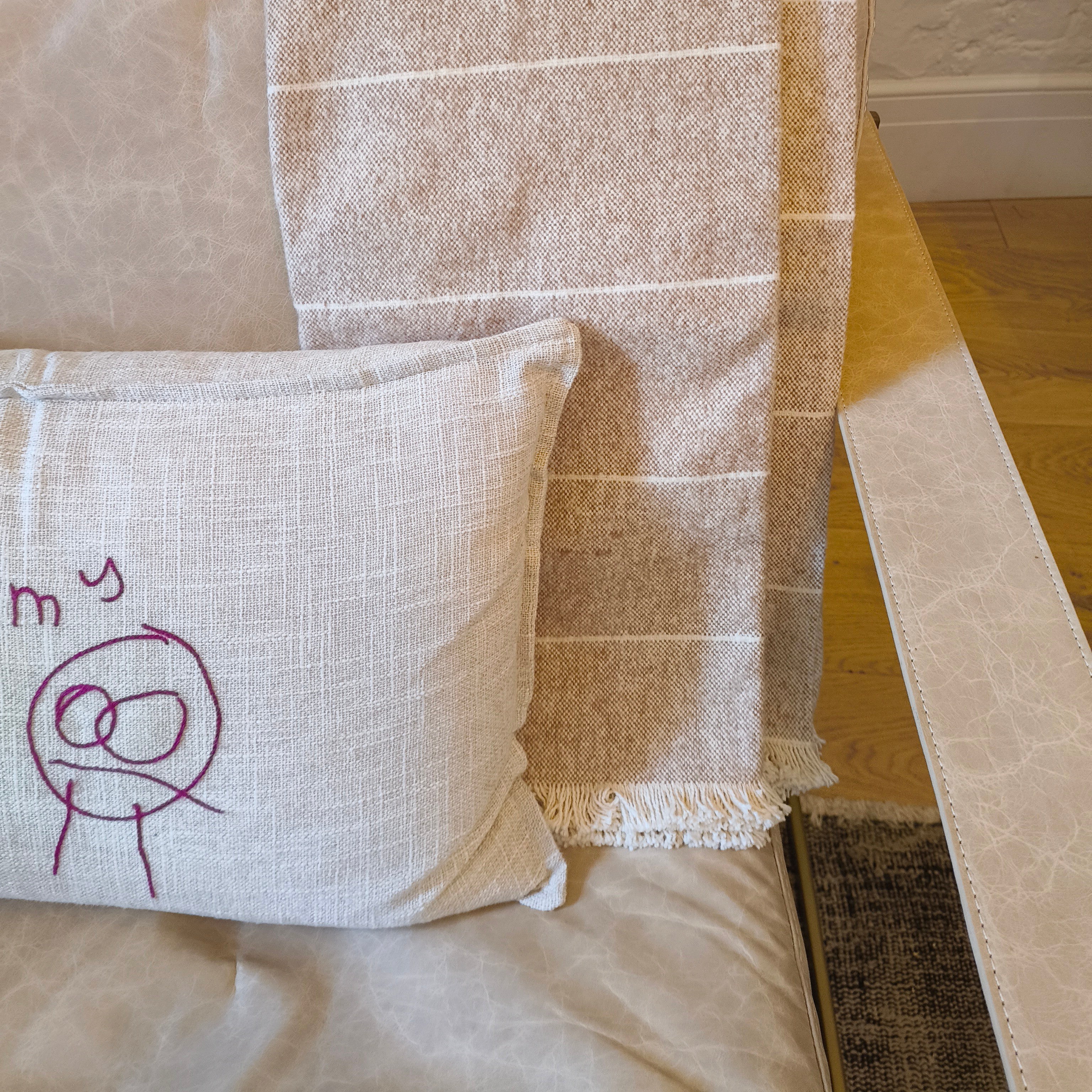 clay coloured striped blanket draped over a chair with a white pillow featuring a stick figure drawing.