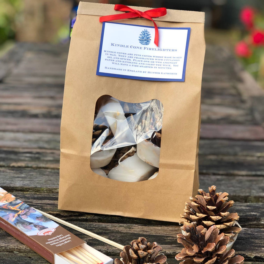 Pine cone candles with matches and a branded paper bag on a wooden surface.
