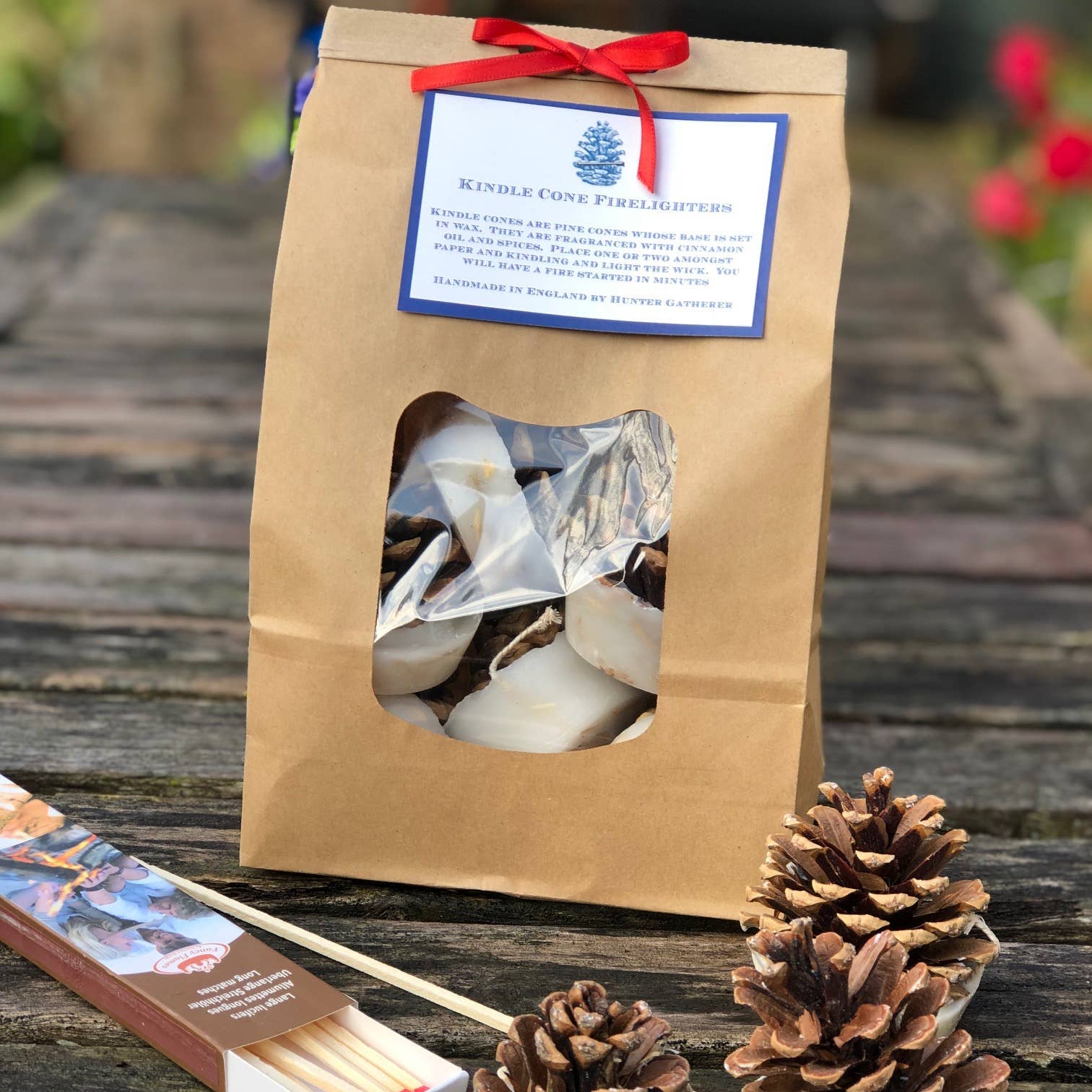 Pine cone candles with matches and a branded paper bag on a wooden surface.
