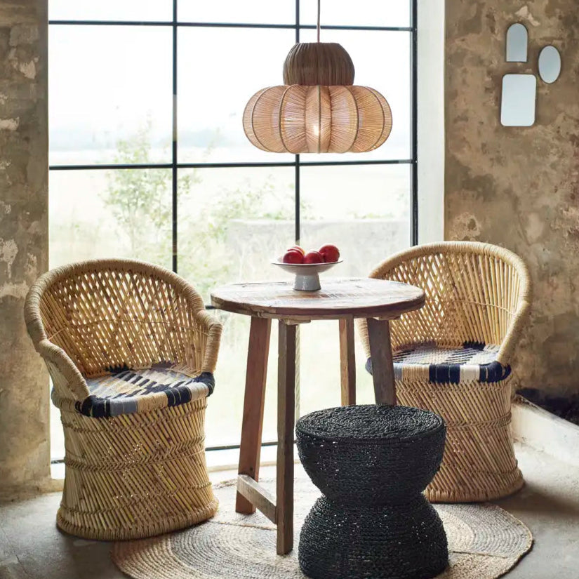 Rattan chairs and table with a black stool in a room with large windows.