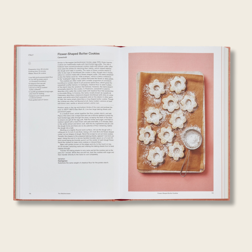 Open cookbook showing a page with flower-shaped butter cookies on a wooden board.