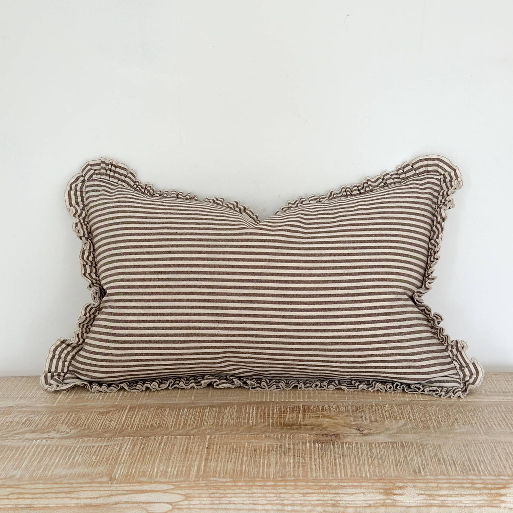 Striped pillow with ruffled edges on a wooden surface against a white wall