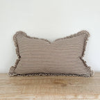 Striped pillow with ruffled edges on a wooden surface against a white wall