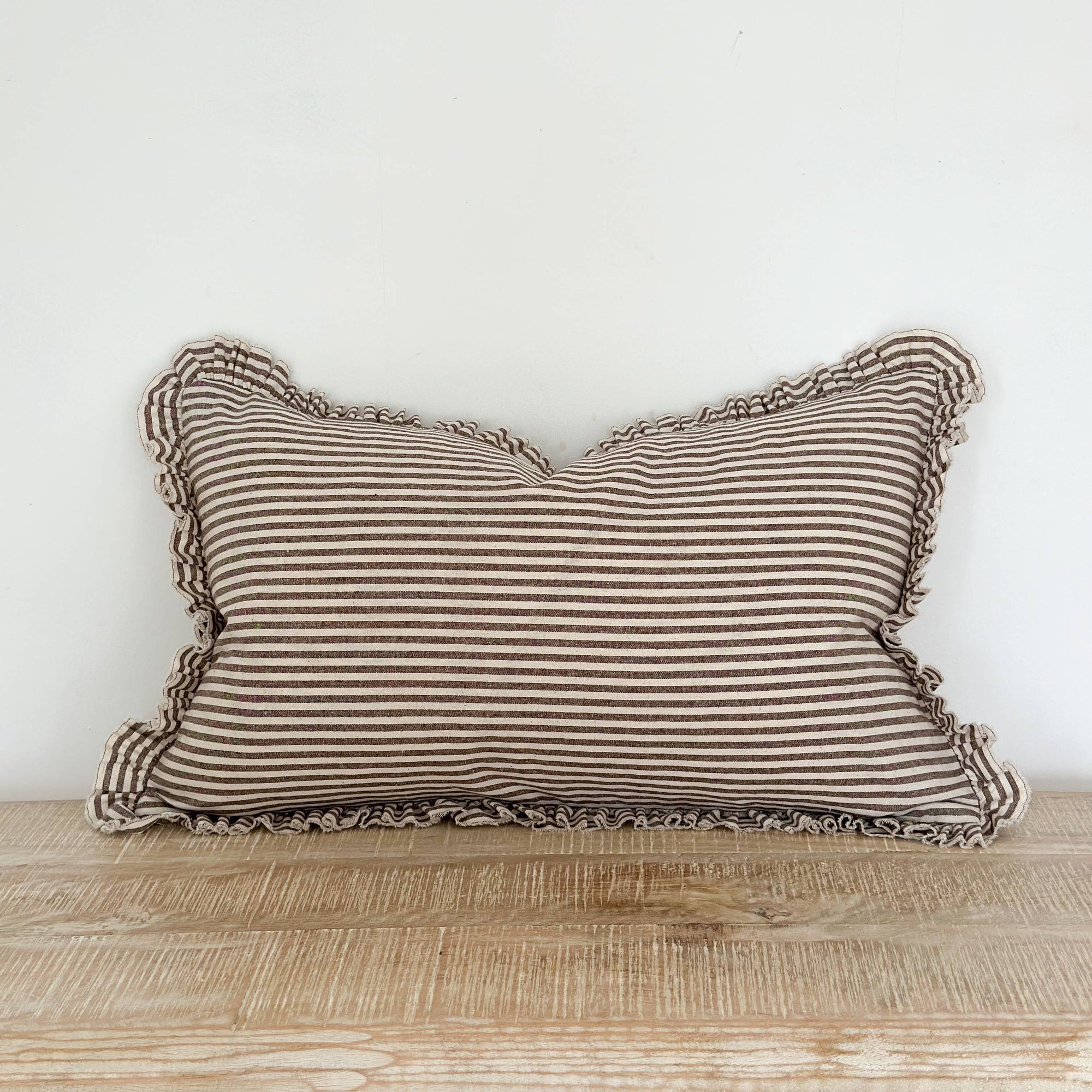 Striped pillow with ruffled edges on a wooden surface against a white wall