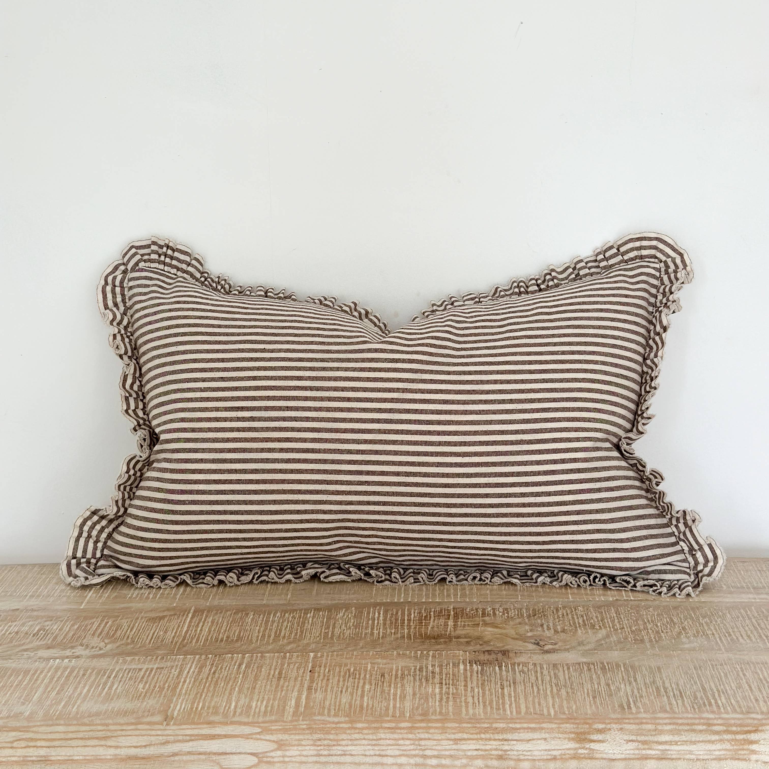 Striped pillow with ruffled edges on a wooden surface against a white wall