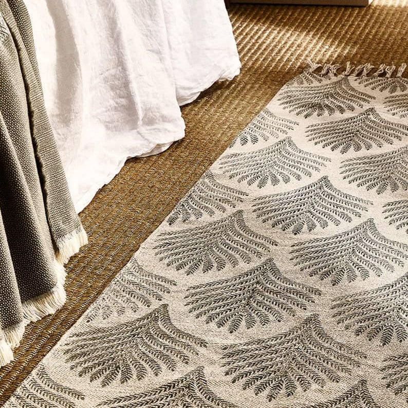 Patterned rug on a jute floor next to a bed with white bedding and a gray blanket.