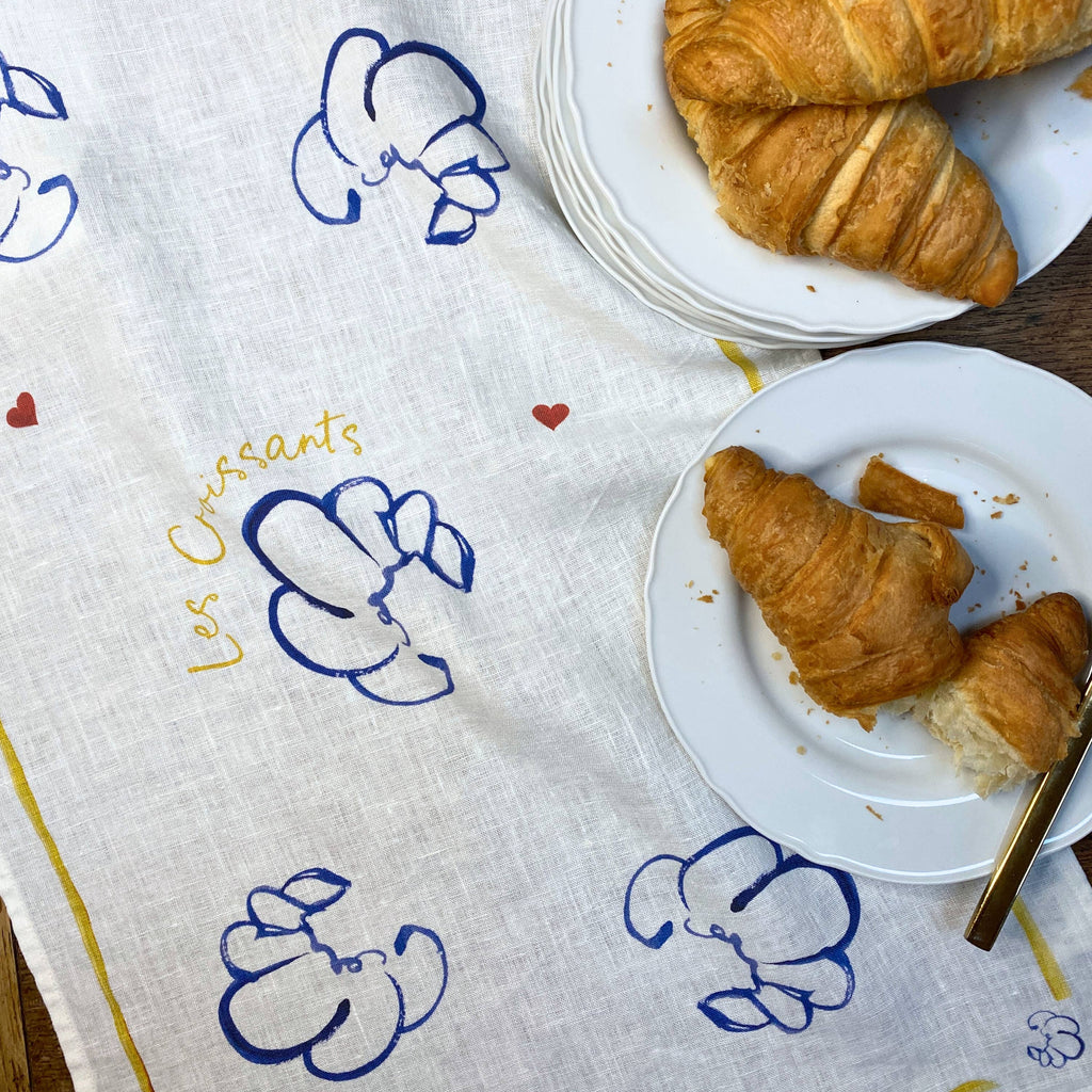 Two plates of croissants on a decorative cloth with 'Les Croissants' text.