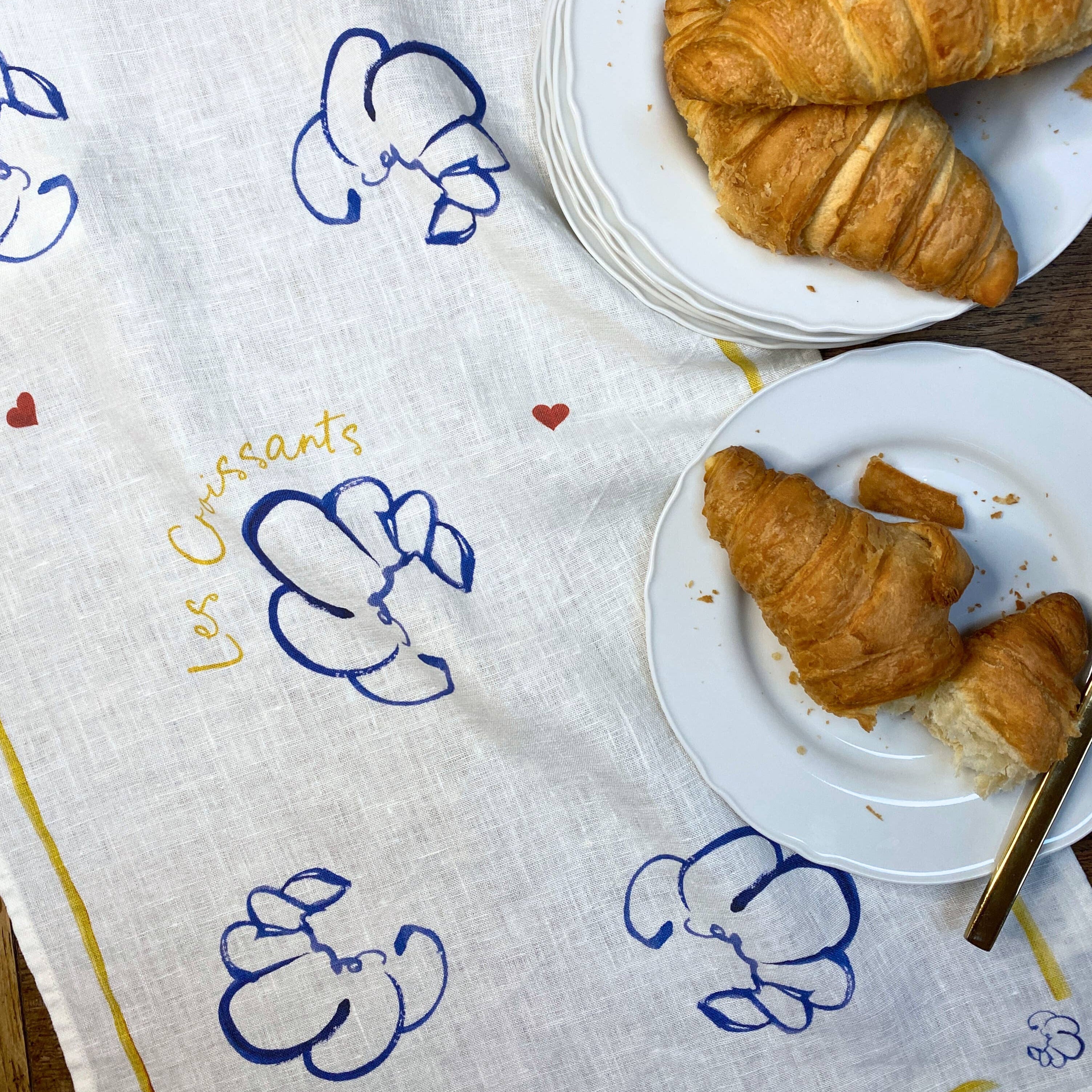 Two plates of croissants on a decorative cloth with 'Les Croissants' text.