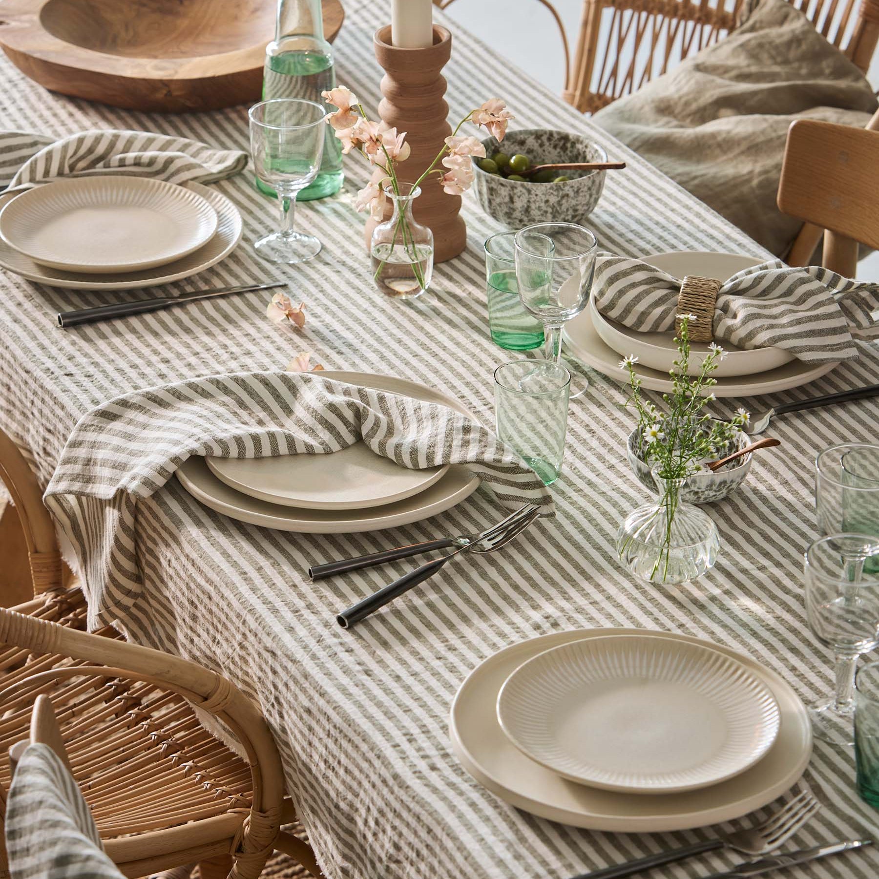Dining table set with plates, glasses, and cutlery on a striped tablecloth.