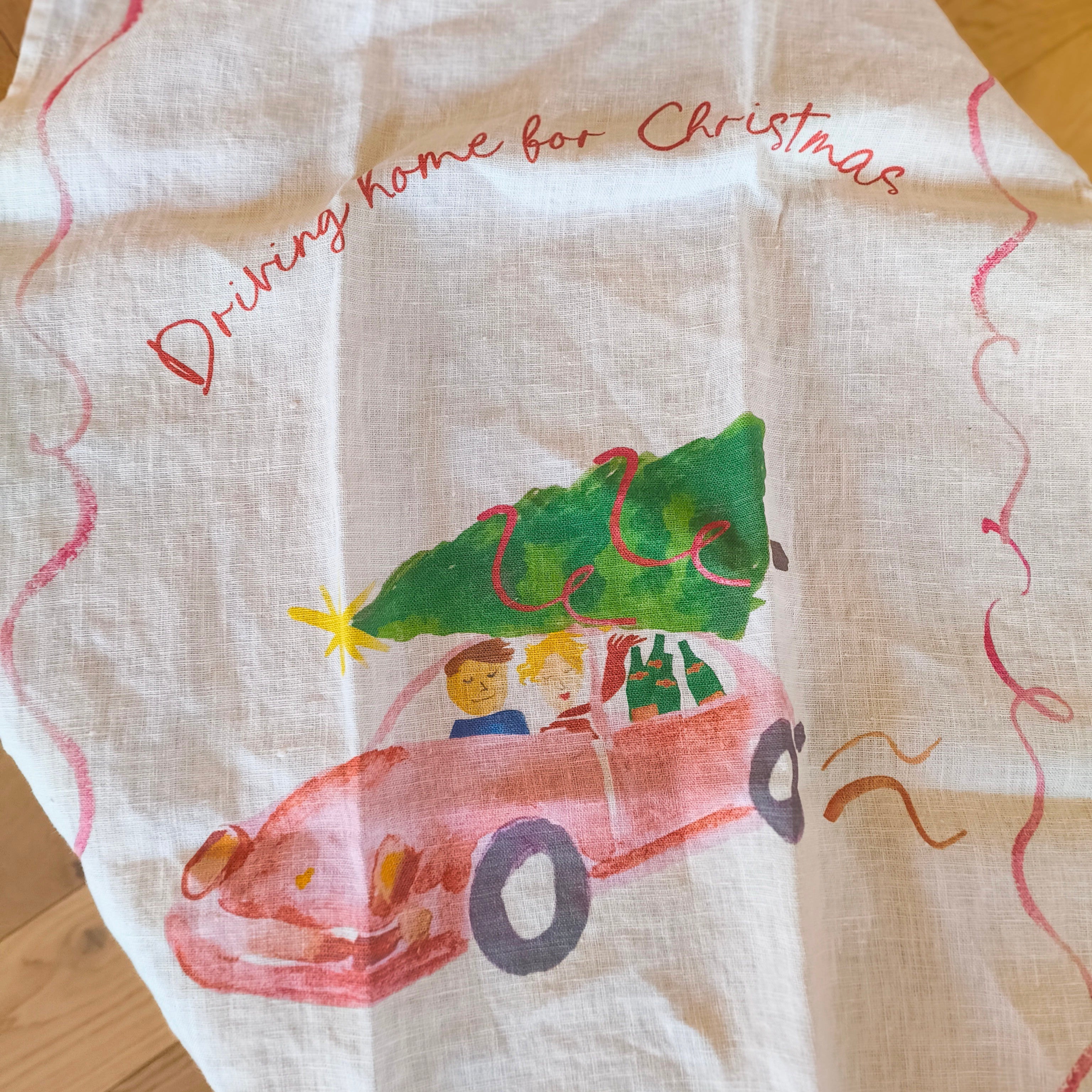 Fabric with a Christmas-themed design of a car carrying a tree and text 'Driving home for Christmas'.