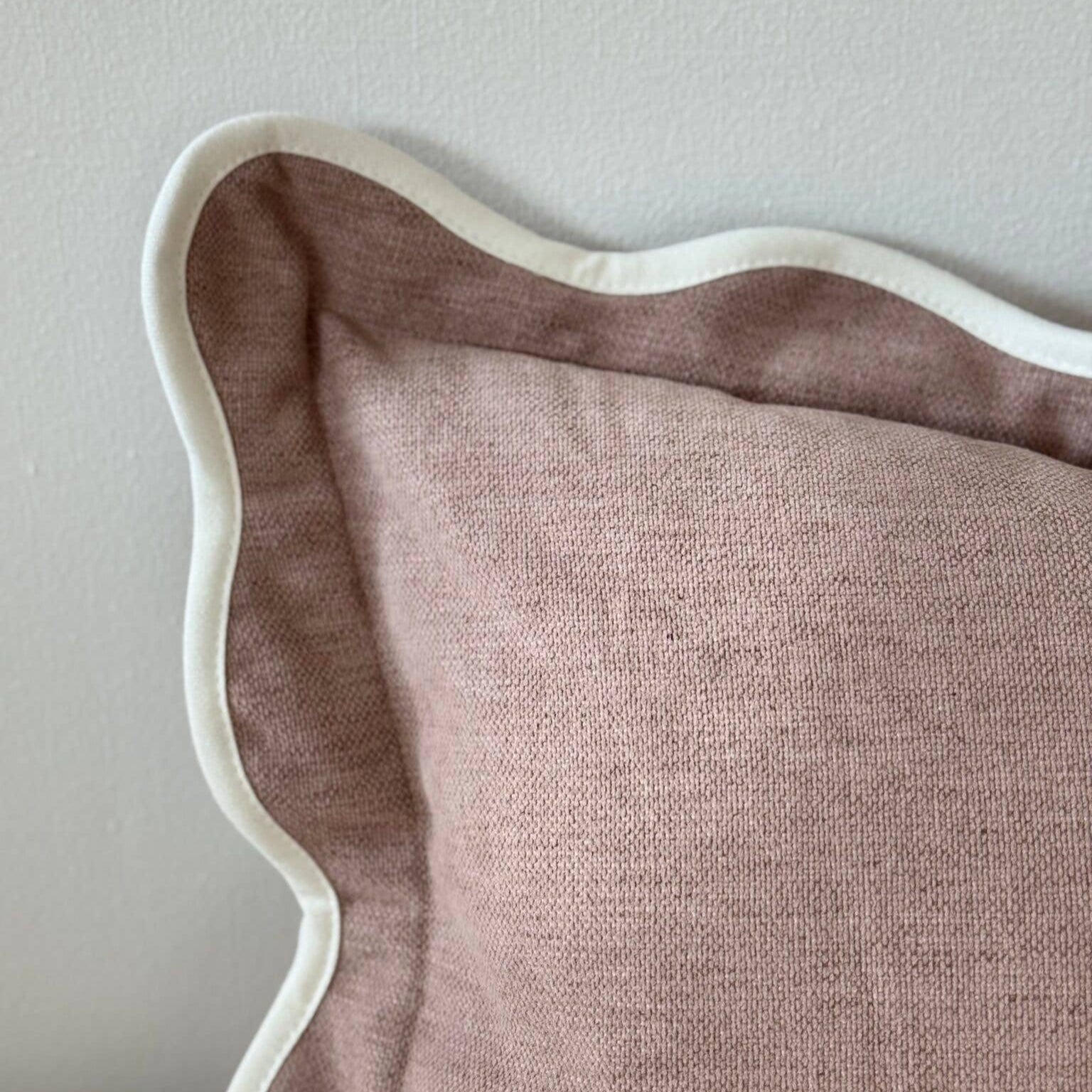 Close-up of a dusk pink pillow with white trim on a neutral background