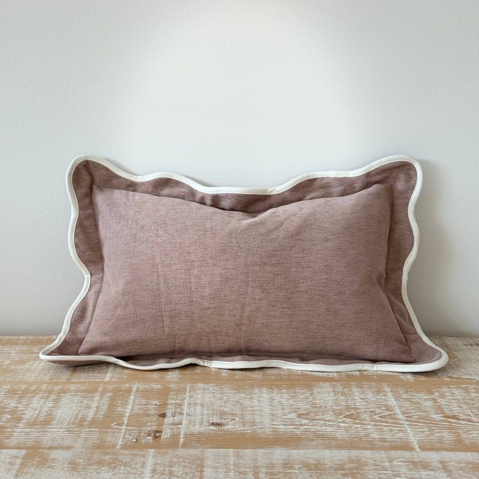 dusk pink pillow with scalloped edge on a wooden surface against a white wall