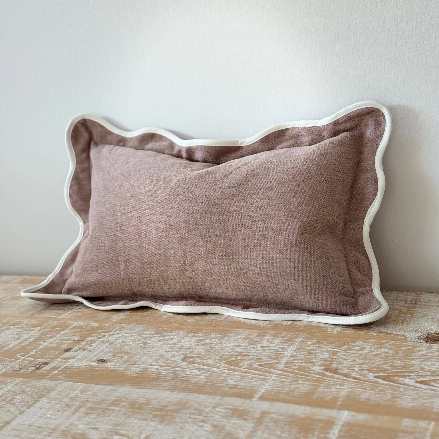 Soft dusk pink pillow with white trim on a wooden surface against a light gray wall