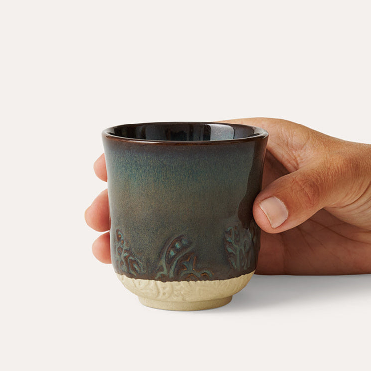 Hand holding a ceramic cup with a textured surface on a light background