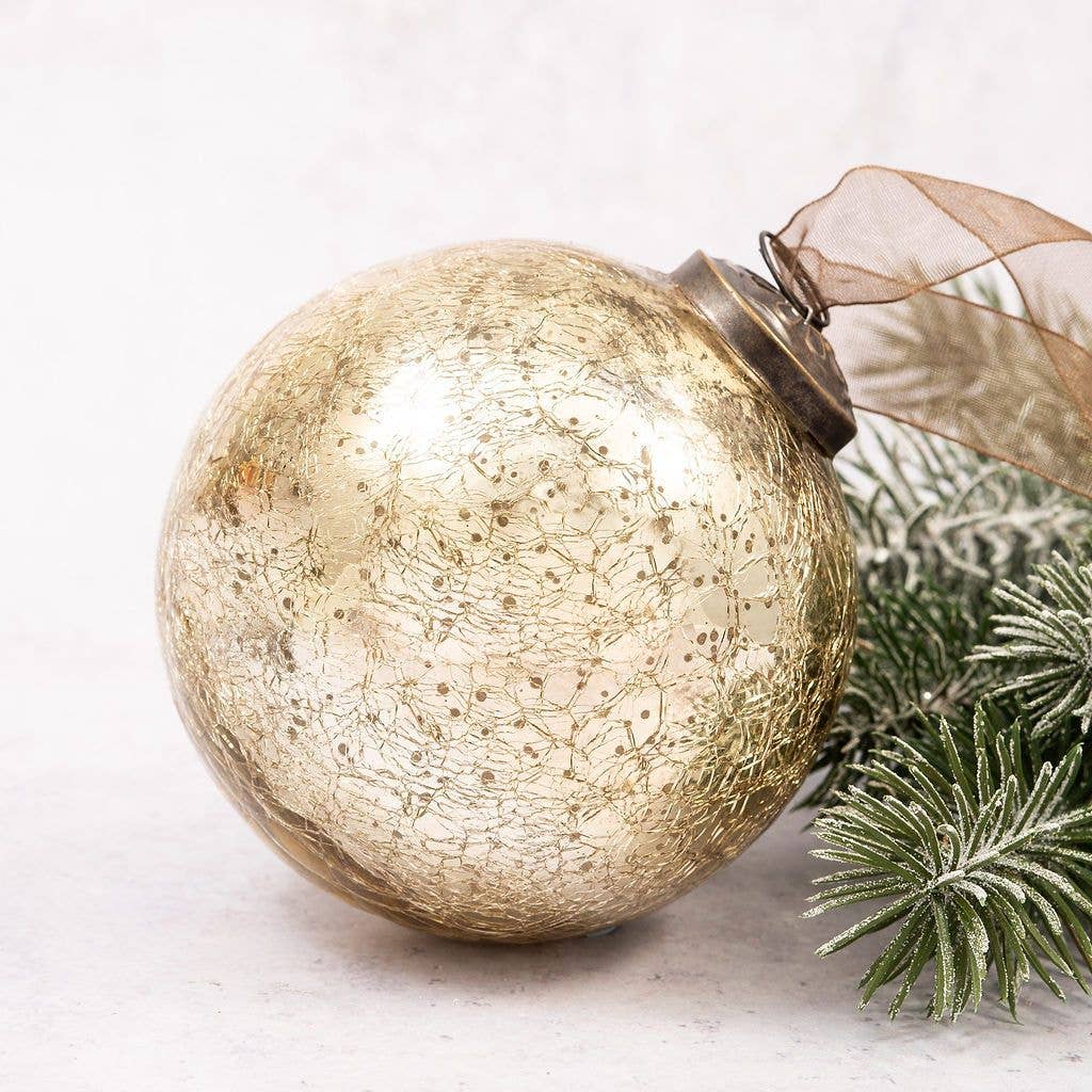 Gold Christmas ornament with textured surface and ribbed texture, attached to a branch on a light background