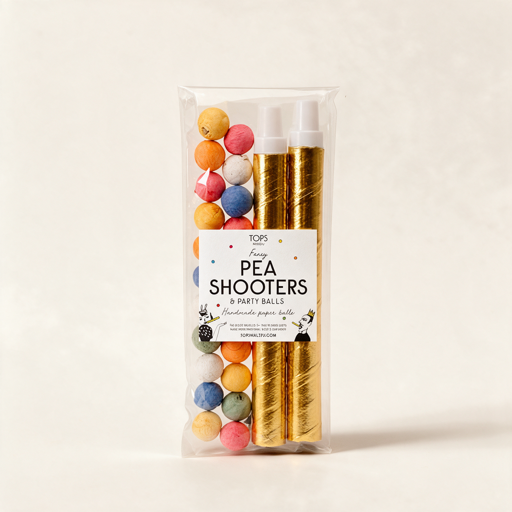 Pair of golden pea shooters with coloured paper balls on a warm cream background