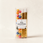Pair of golden pea shooters with coloured paper balls on a warm cream background