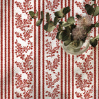 Red floral patterned fabric with a glass vase and greenery on a white background