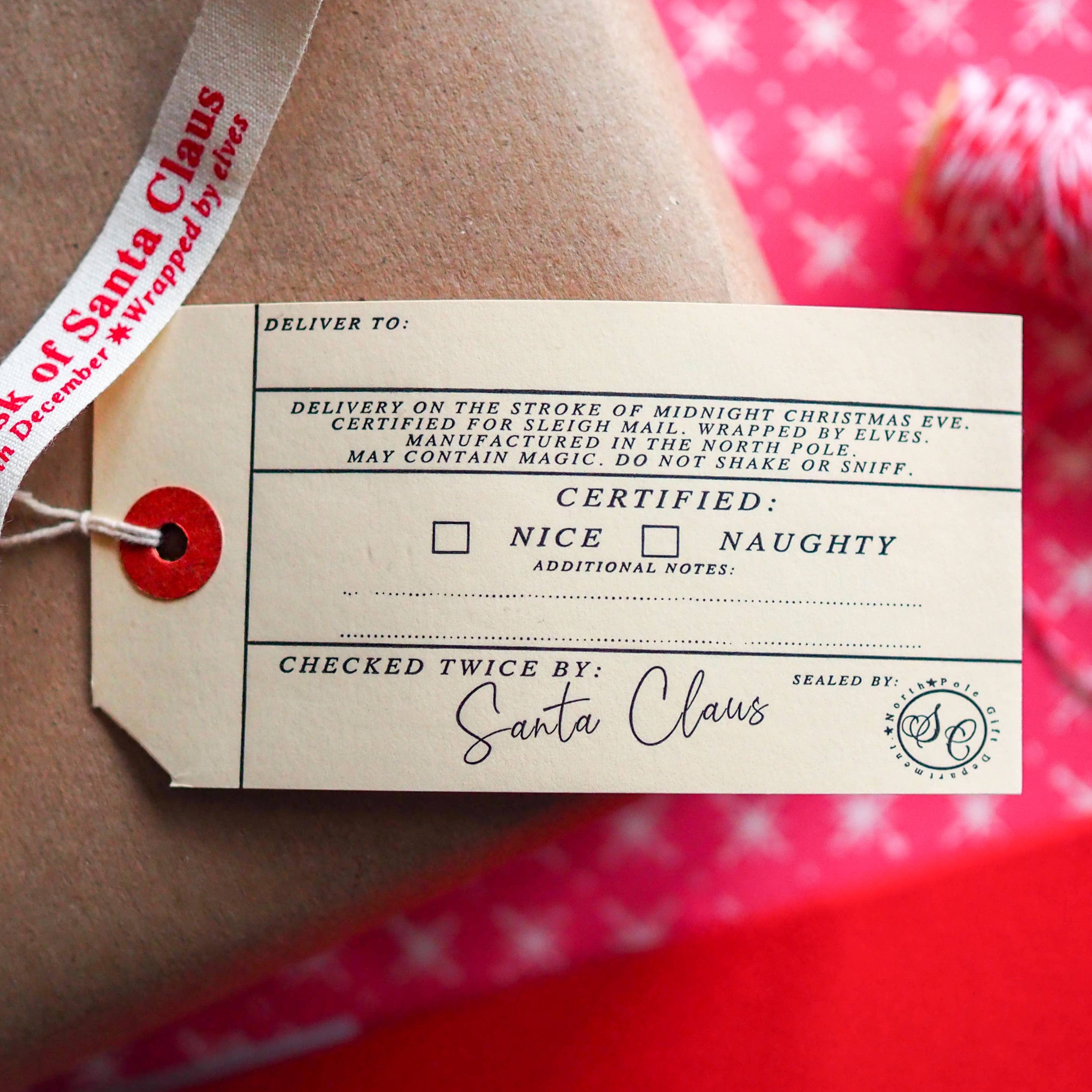 Gift tag with Santa Claus certification on a wrapped present with red ribbon.