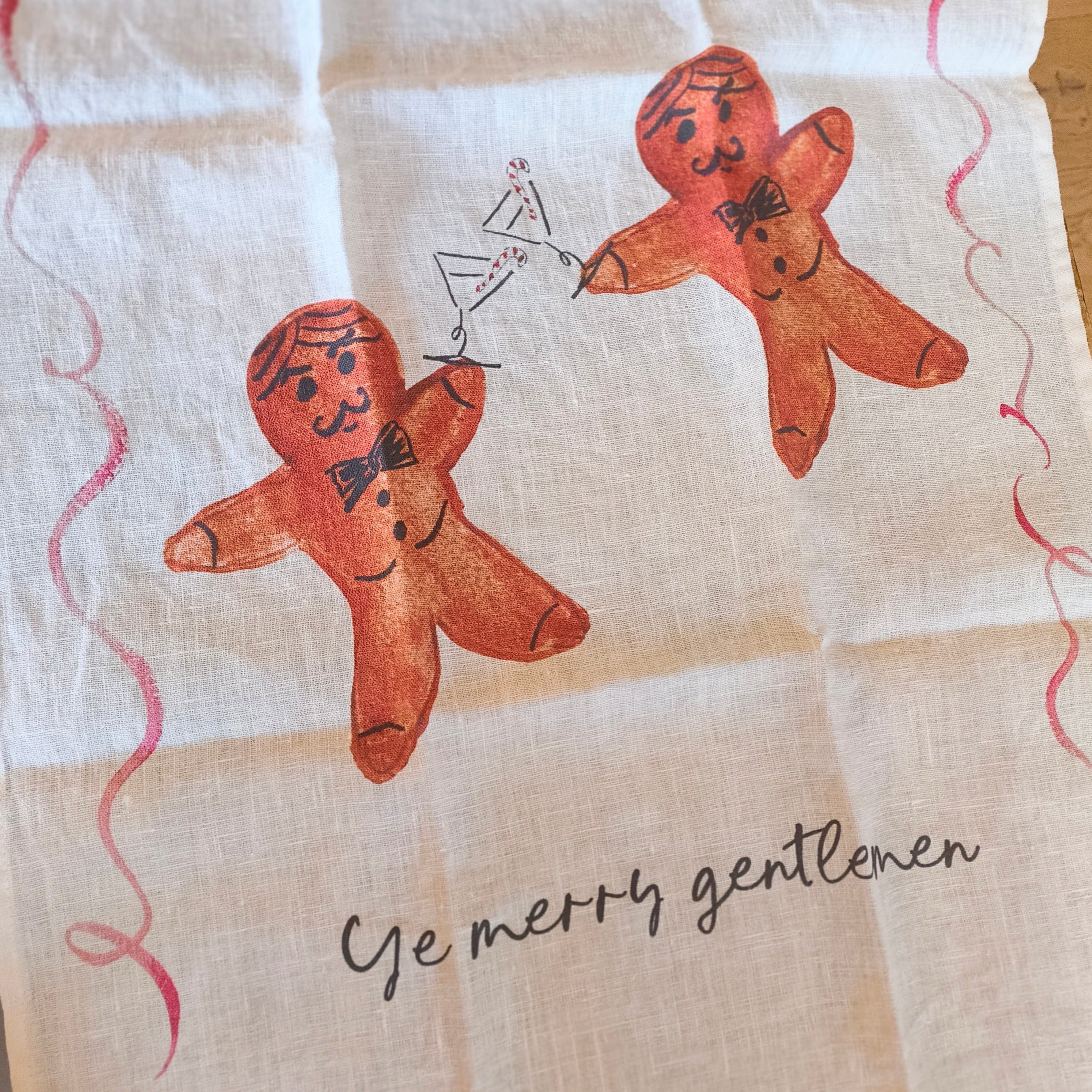 Tea towel with gingerbread men and text 'Ye merry gentlemen' on a wooden surface
