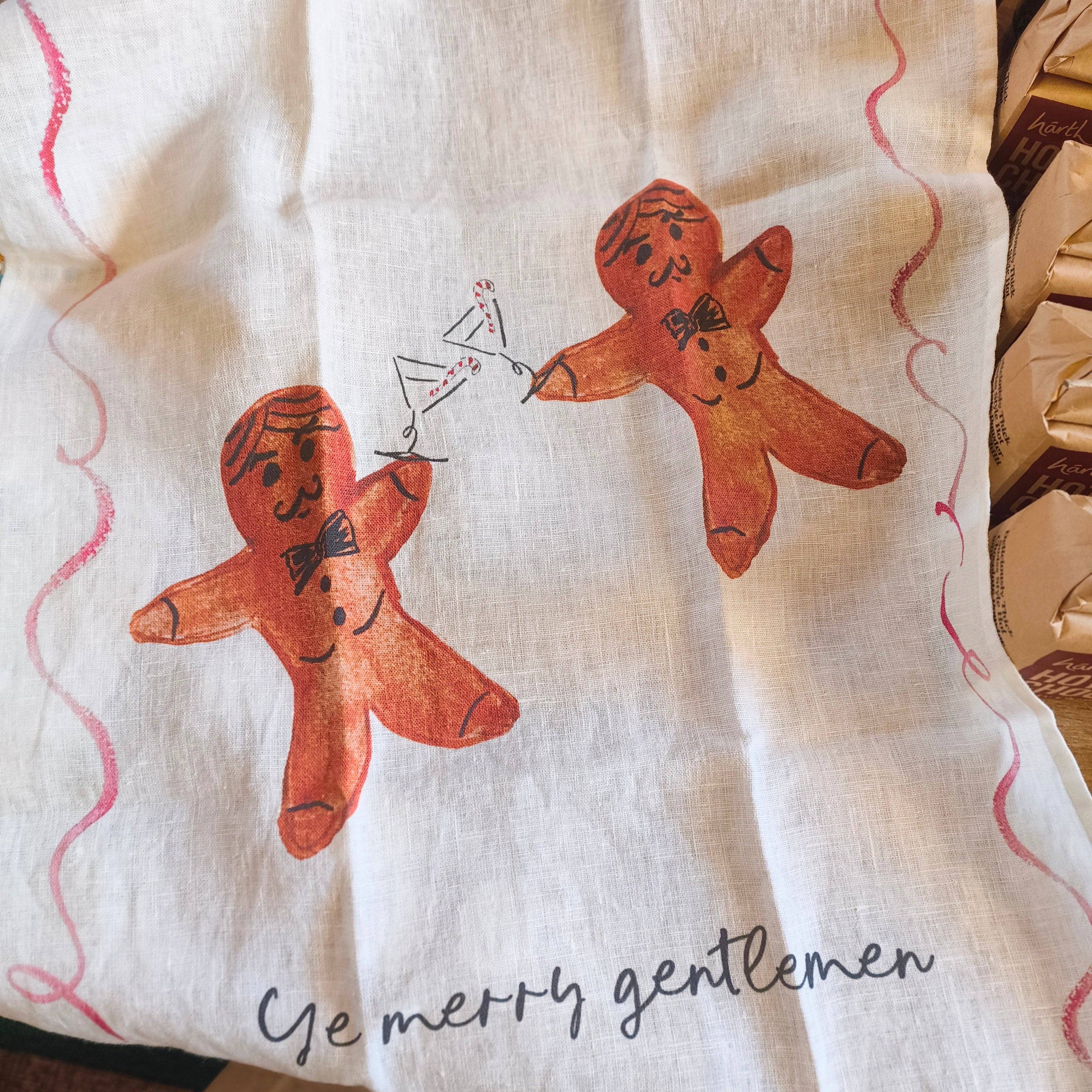 Fabric with gingerbread men design and text 'Ye merry gentlemen' on a wooden surface.