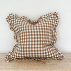 Brown and white checkered pillow with ruffled edges on a wooden surface.
