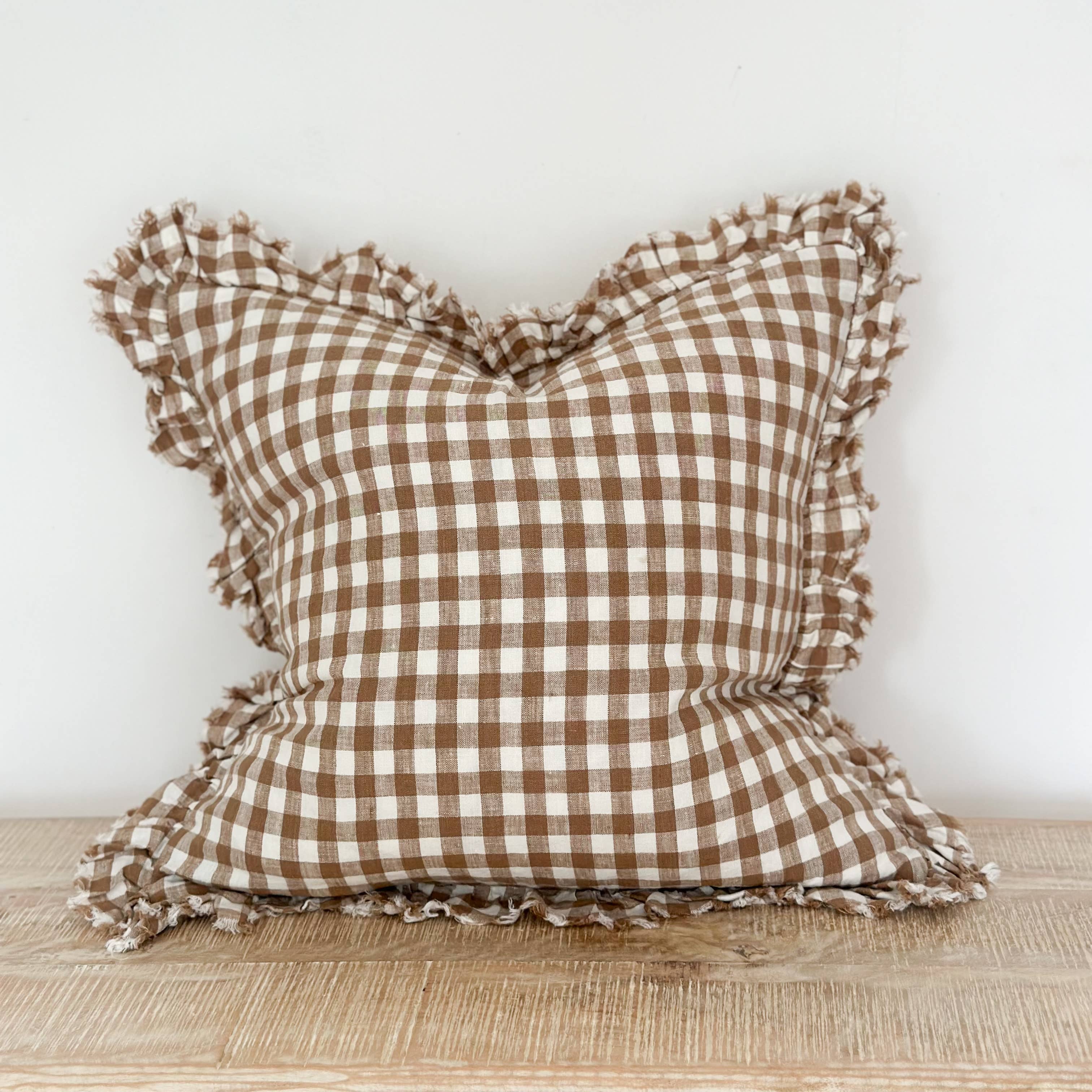 Brown and white checkered pillow with ruffled edges on a wooden surface.